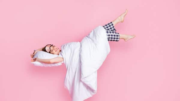 Graphic of a woman lying in bed in her pajamas on a pink background.