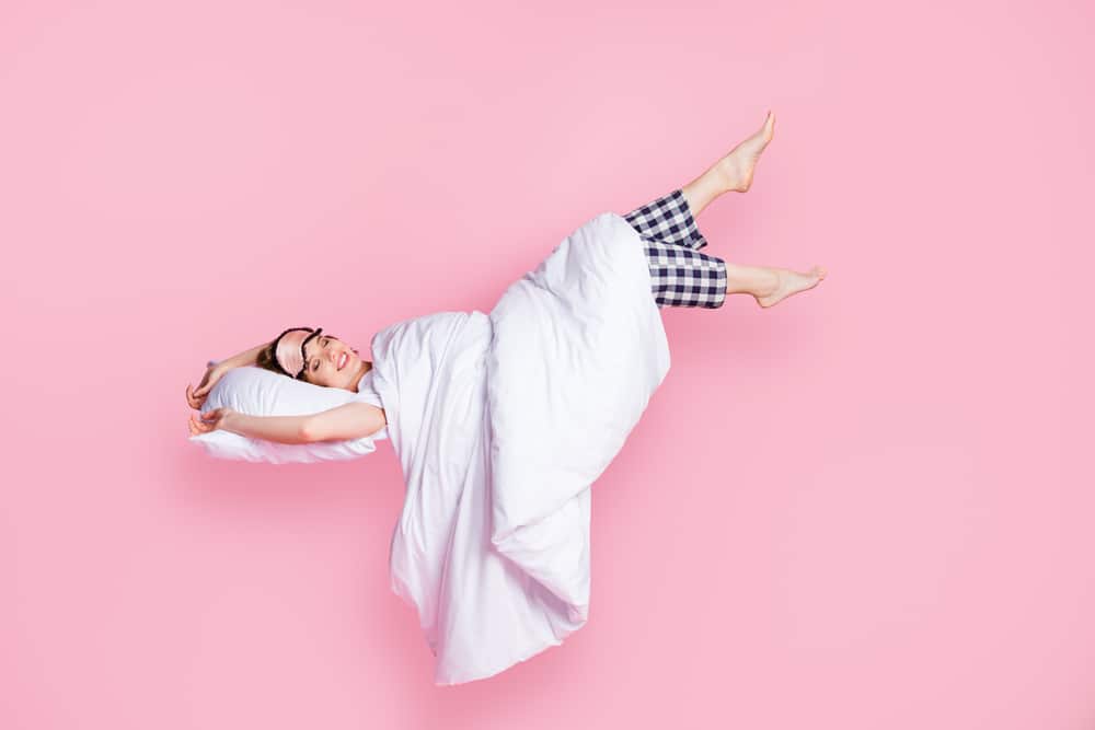 Graphic of a woman lying in bed in her pajamas on a pink background.