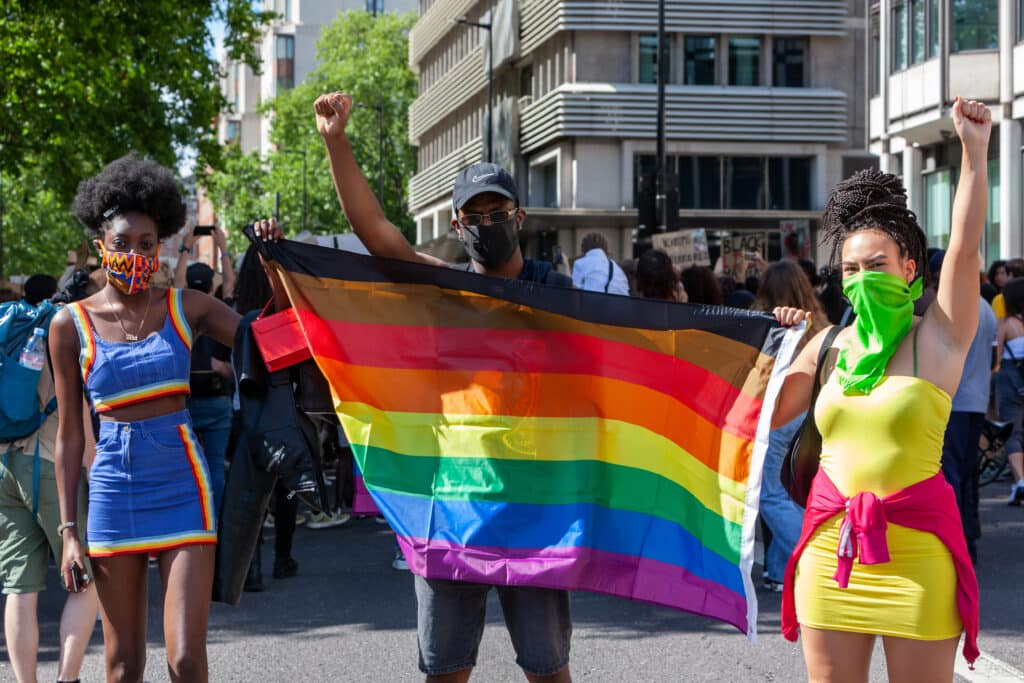 Three people carrying a Pride flag at BLM march in London.