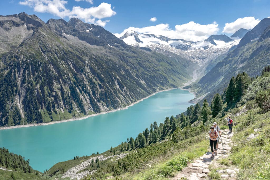 Hikers going uphill on a path next to a river and mountains.