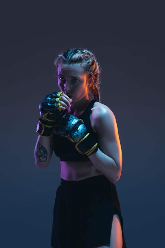 Portrait of Caucasian female fighter isolated over blue background in neon