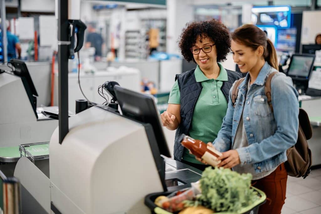A Part-Time supermarket worker helping customer at self checkout