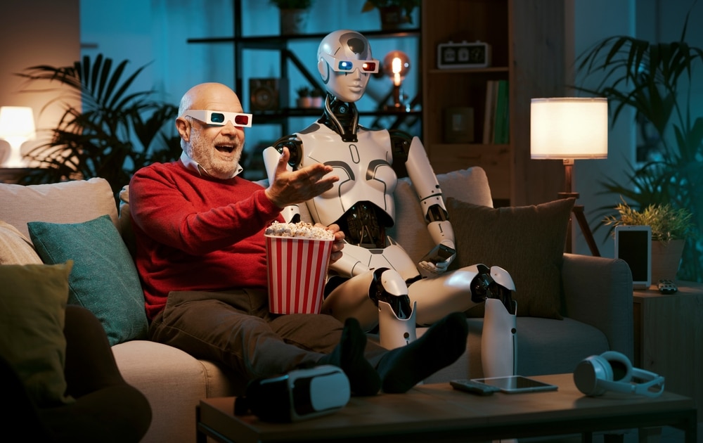 An old man and a robot sit on the couch watching a movie together. They are wearing 3D glasses and eating popcorn.