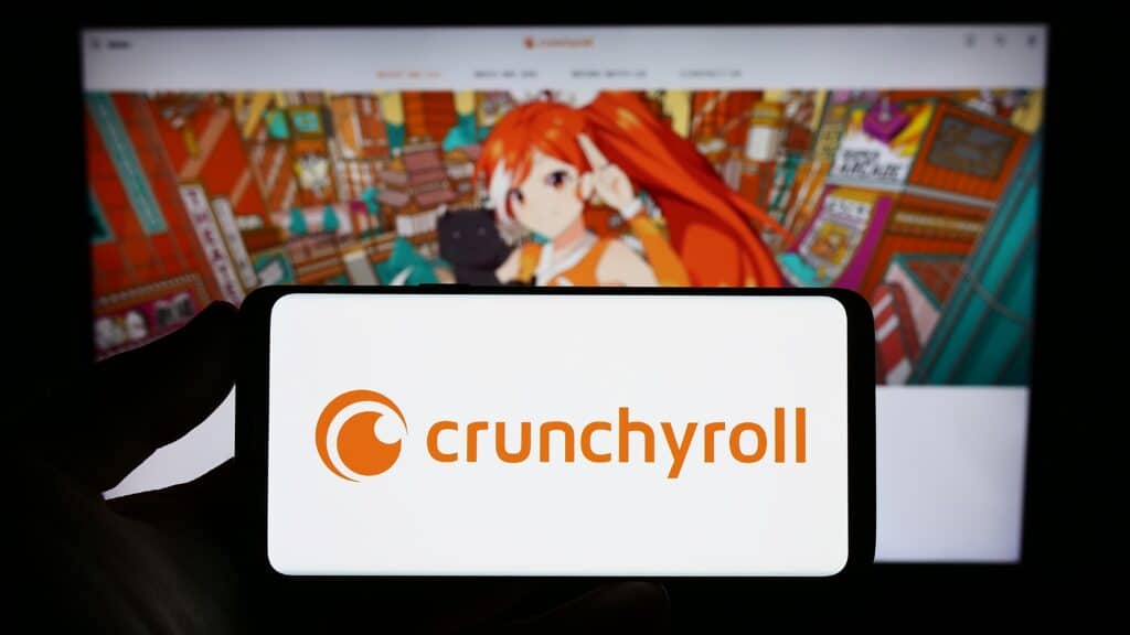 Person holding smartphone with logo of US entertainment company Crunchyroll LLC on screen in front of website. Focus on phone display. Unmodified photo.