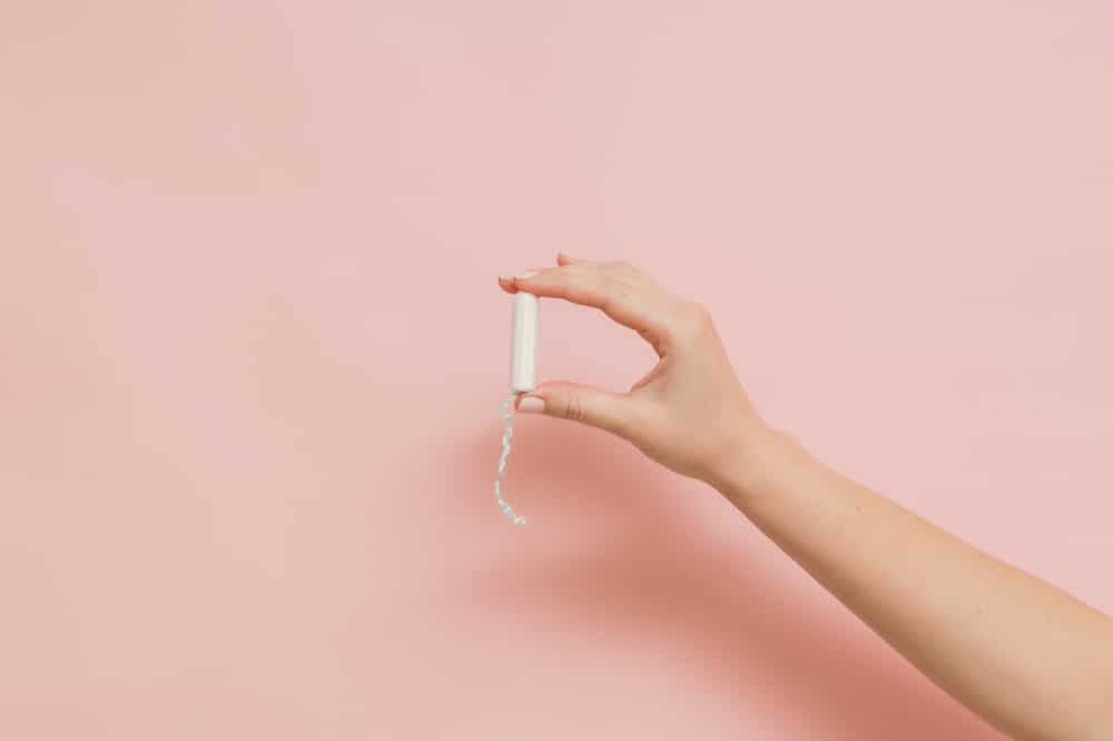 Hand holding a tampon. Light pink background.