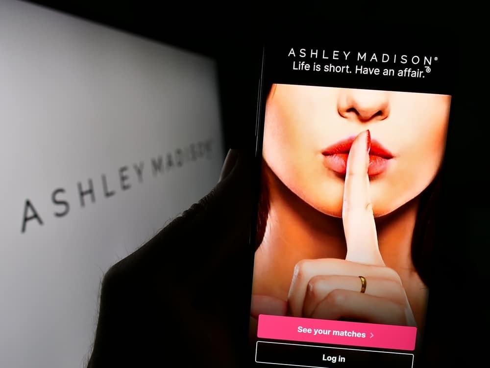 Phone screen with the Ashley Madison promo of a woman holding her finger up and shushing beneath the "life is short, have an affair" tagline.