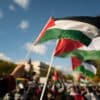 A hand holding up a Palestinian flag that flows in the wind in the middle of a crowd.