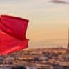 A French flag branding the 2024 Olympics' logo flies in the forefront of an out-of-focus photo of Paris and the Eiffel Tower.
