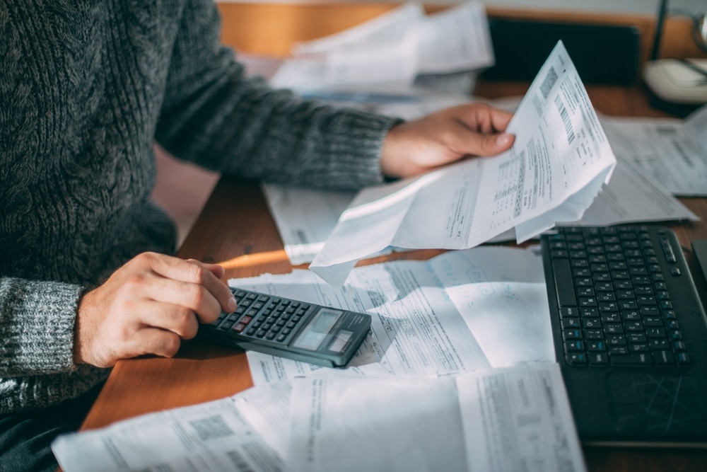A close up of hands dealing with uni house utility bills with lots of papers and a calculator on the table.
