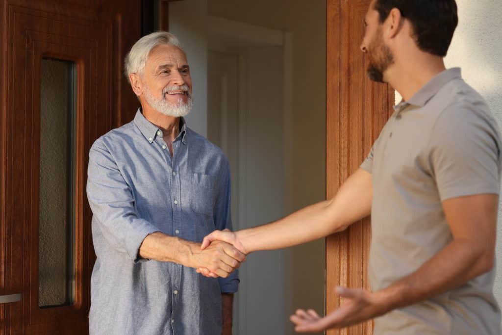 Two neighbours shaking hands and being friendly in the doorway of a house.