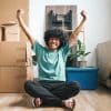 A young man celebrating moving into his uni house with boxes behind him.
