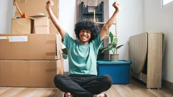 A young man celebrating moving into his uni house with boxes behind him.
