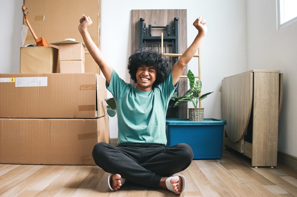 A young man celebrating moving into his uni house with boxes behind him.