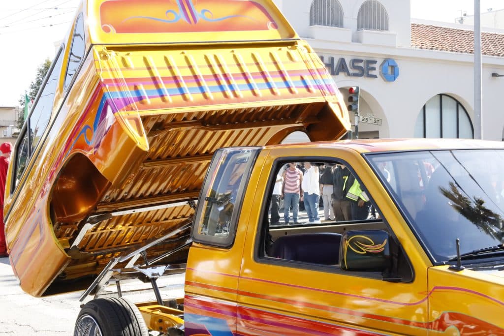 Bright yellow with other colors- truck style lowrider, back of tuck raised in the air.