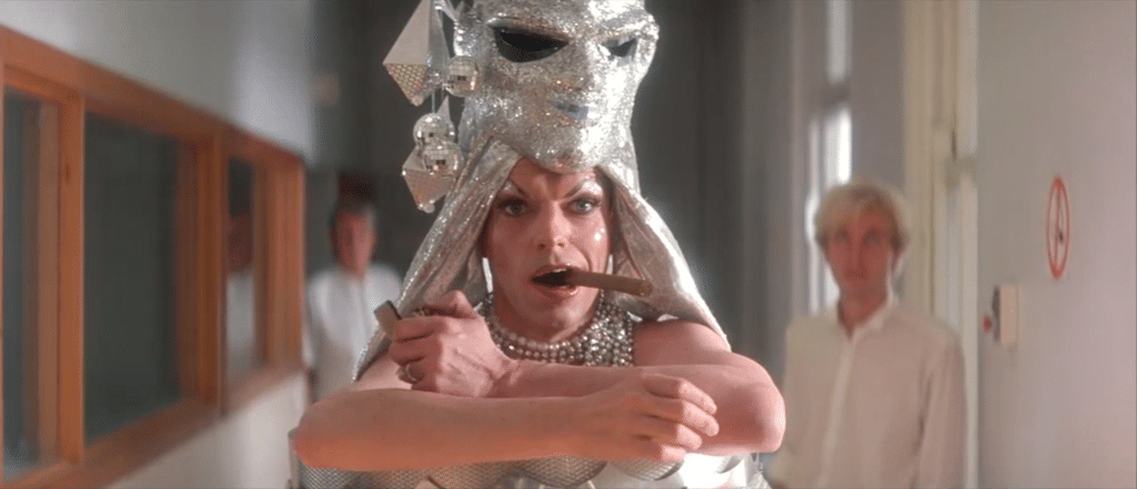 A man in drag, standing in a hospital waiting room. He is lighting a cigar. Hugo Weaving in 'Priscilla, Queen of the Desert'