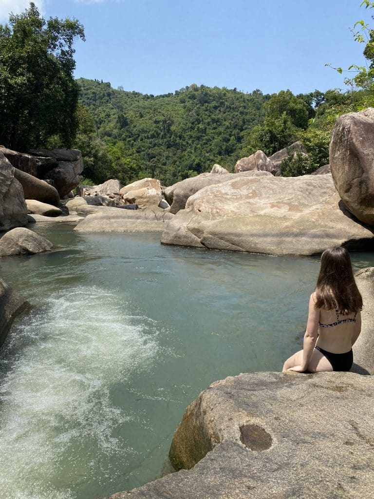 A girl sitting on a rock in front of a body of water