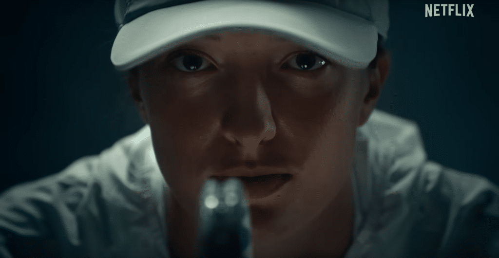 Iga Swiatek in 'Break Point'. She is looking directly at the camera with a racquet covering the lower half of her face.