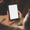 Lady laying on couch reading on her e-reader. Close up of hands and e-reader. View from behind.