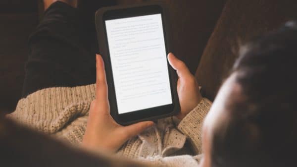 Lady laying on couch reading on her e-reader. Close up of hands and e-reader. View from behind.