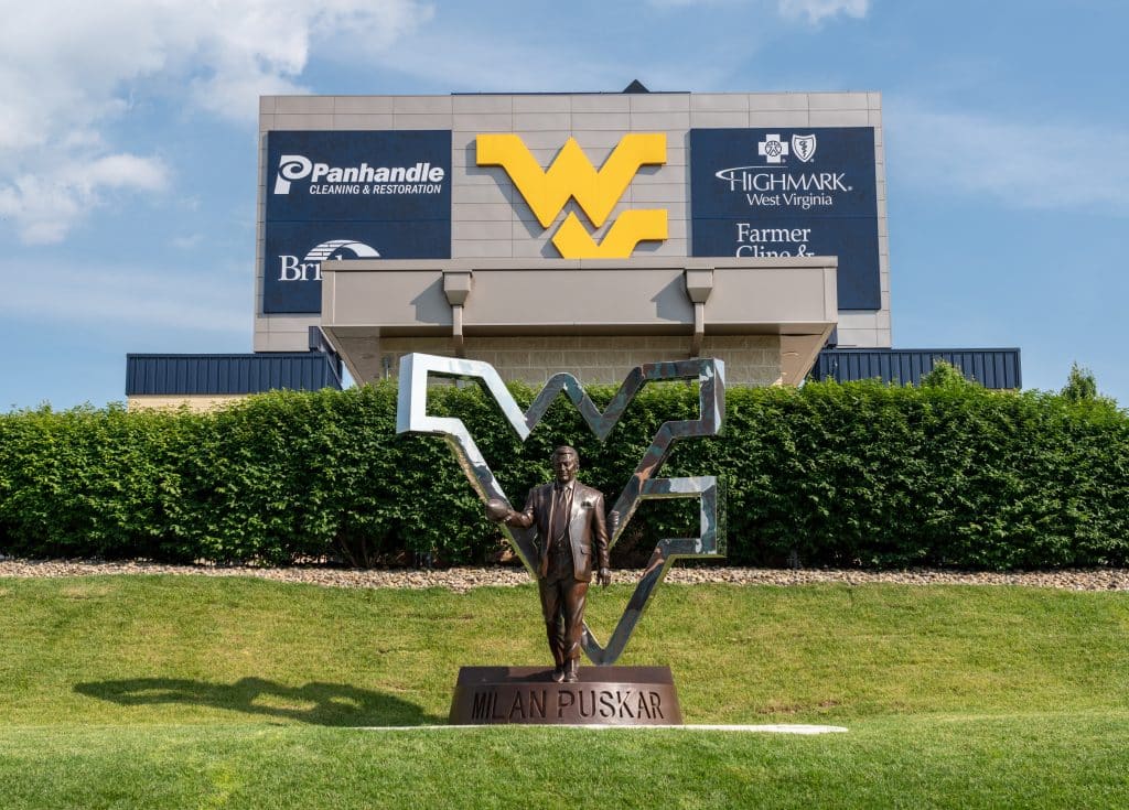A statue of Milan Puskar, in front of West Virginia University football stadium on a sunny day.