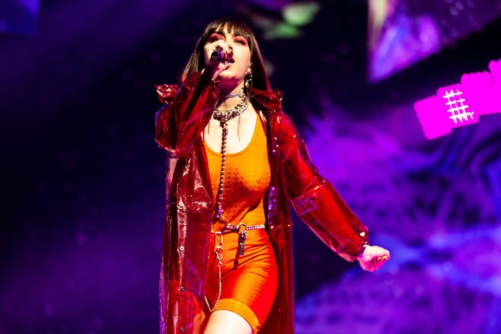 Charli XCX performing on stage in an orange outfit