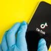 Hands in medical gloves holding a phone that displays TikTok where Gen Z receives their heal information.