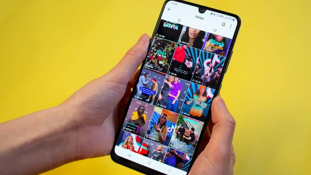 Two hands hold a phone showing a feed of videos on TikTok