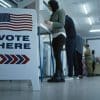 Various people voting with a "Vote Here" sign displayed.