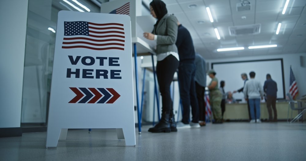 Various people voting with a "Vote Here" sign displayed.