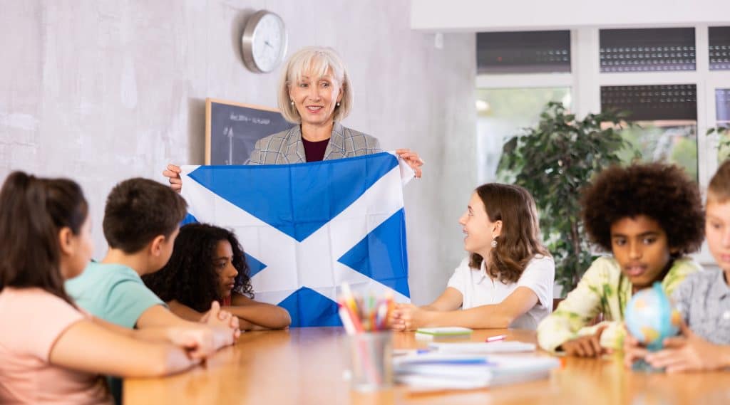 A teacher shows a Scottish flag to pupils