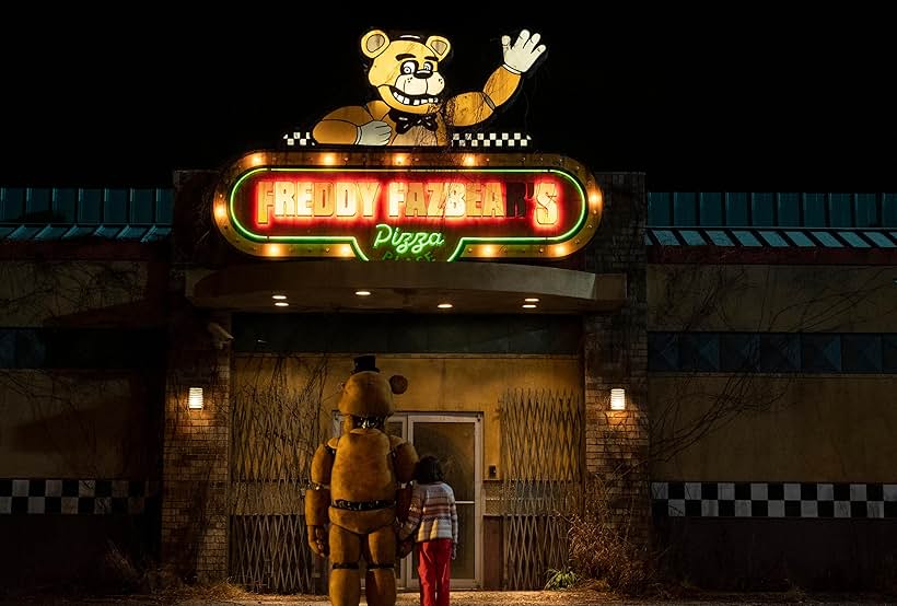Still from 2023 Five Nights at Freddy's film showing exterior of the restaurant 'Freddy Fazbear's Pizza' lit up on a neon sign