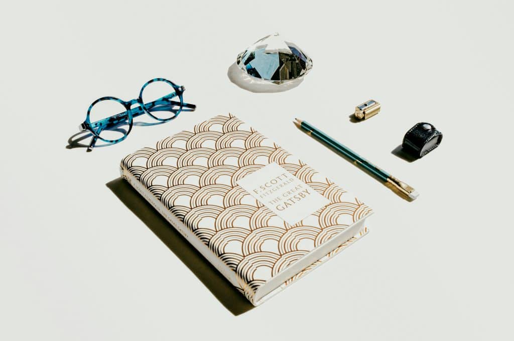 A copy of the Great Gatsby, along with glasses, a pencil, and other supplies
