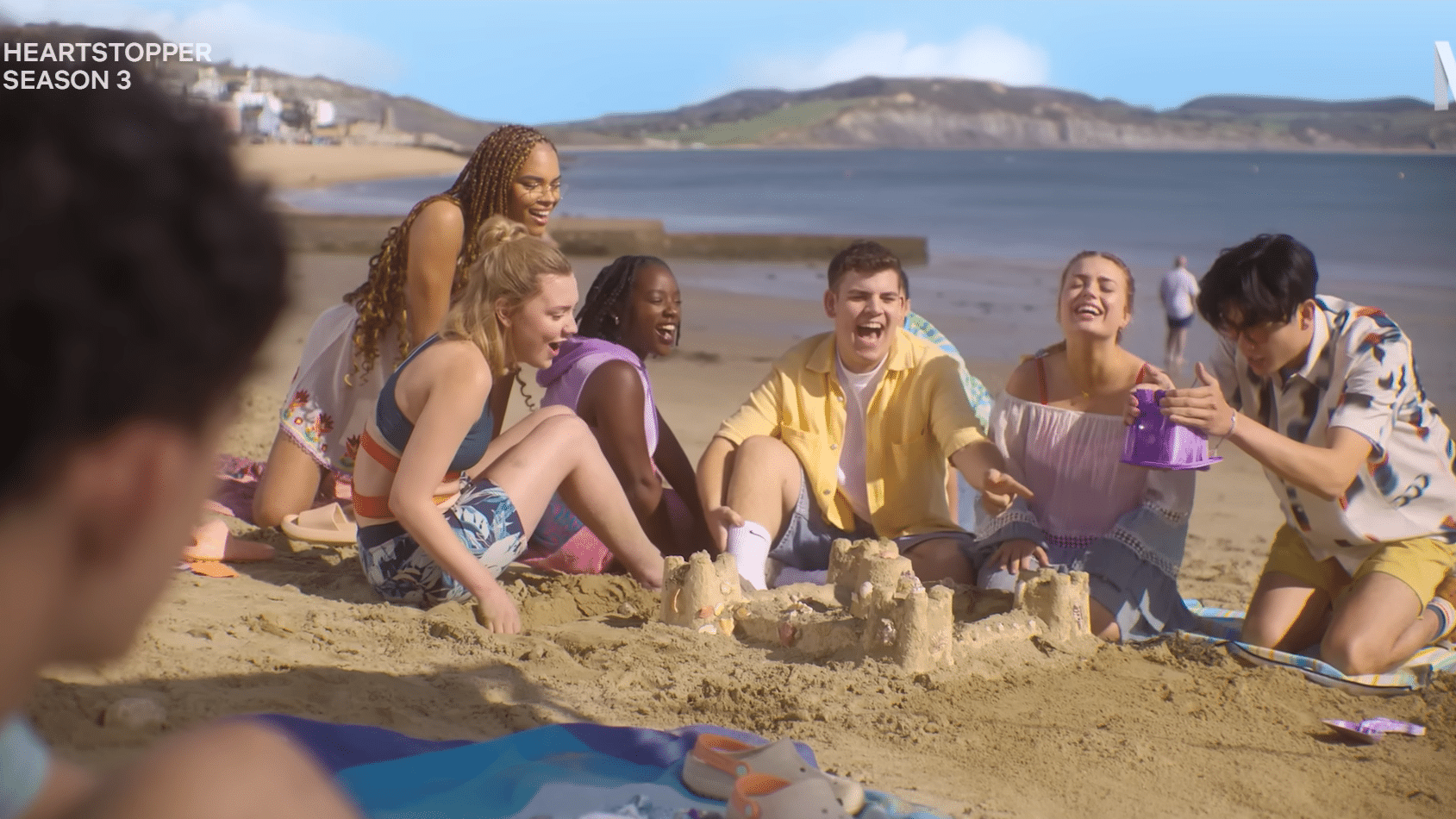 The Heartstopper group together on the beach as Charlie watches.