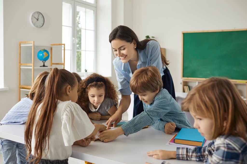 Woman teaching a small group of elementary students around a table.