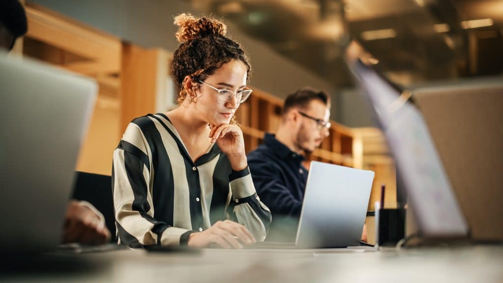 Woman working on laptop next to coworkers.