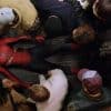 An unmasked Spider-Man lies on a train floor as people surround him