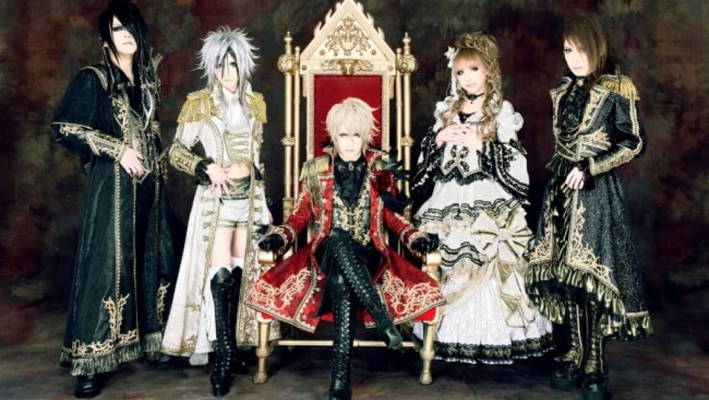 Visual kei band, Versailles, poses upon a red throne. Each of the five members is dressed in an elaborate, Rococo inspired outfit.