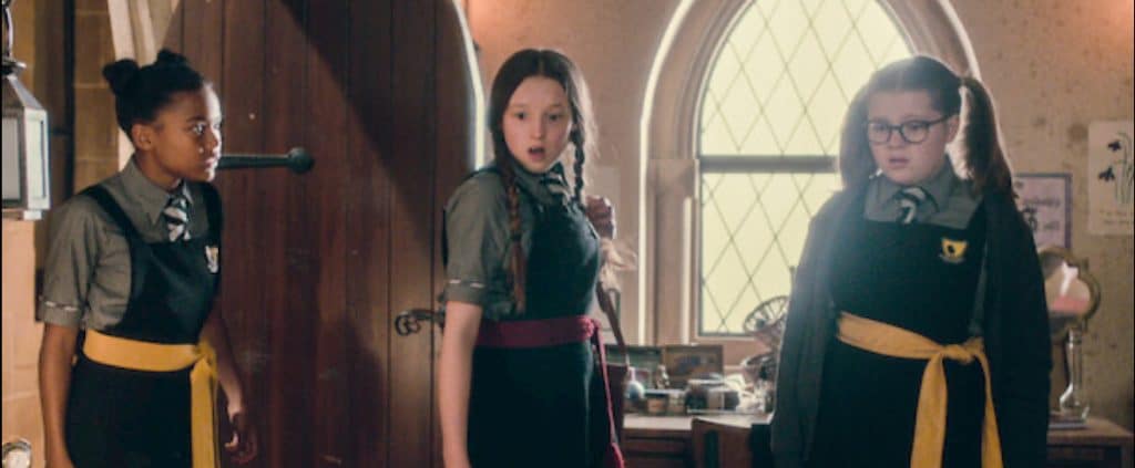 Three girls in school uniforms look at each other in surprise.