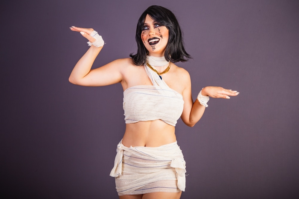 Woman wearing a mummy costume for Halloween. Purple background.