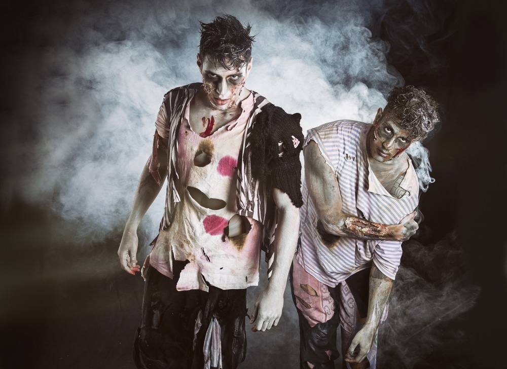 Two male zombies look into the camera. Smoky, black background.