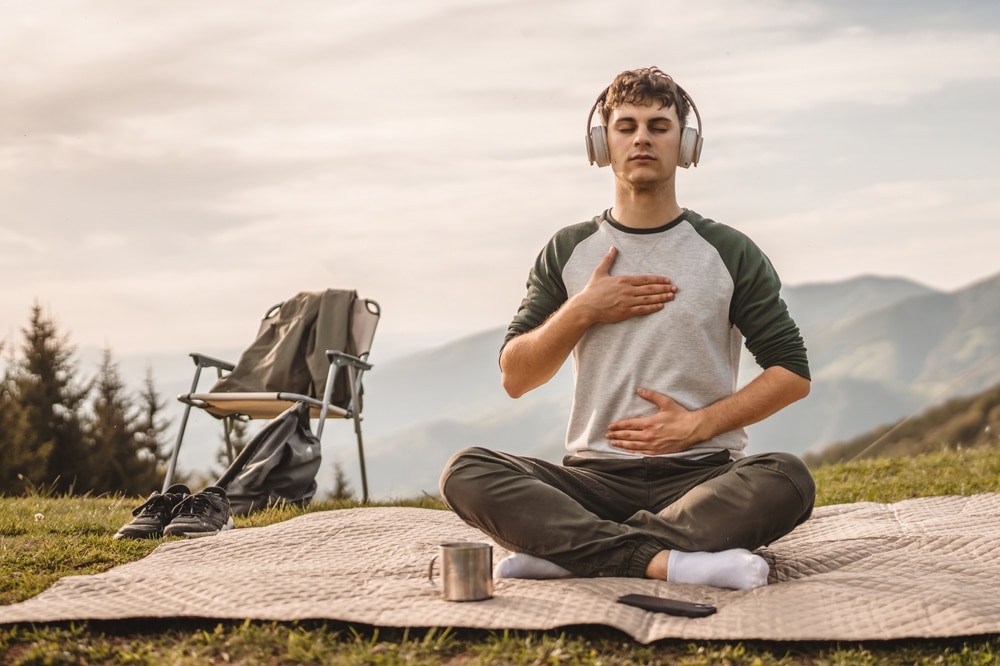 young man with headphones meditating on a mountaintop