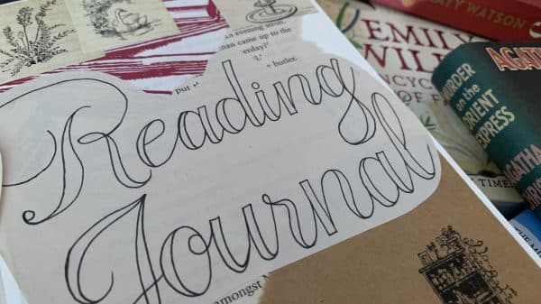 The image shows a collage-style arrangement featuring a "Reading Journal" with the words written in a decorative script on a cut-out piece of paper. Surrounding the journal are various elements, including small vintage-style illustrations of plants and a goose, as well as a red and white patterned piece of paper. In the background, there are several books stacked on top of each other. The visible titles include "The Three Dahlias" by Katy Watson, "Emily Wilde's Encyclopaedia of Faeries," by Heather Fawcett, "Murder on the Orient Express" by Agatha Christie, and "Our Violent Delights" by Chloe Gong. There is also a small illustration of a bookshelf with books on the brown cover of the journal.