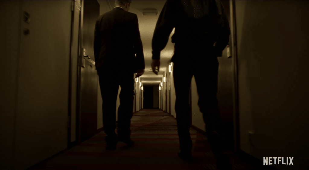 2 men walk down a dimly lit hallway.