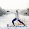 Photo of a woman doing yoga in the snow with a hat and scarf on as winter workout.