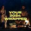 A group of friends sits around a campfire at night, enjoying a peaceful outdoor setting with a tent in the background. One person plays a guitar while others reflect and connect, symbolizing a moment of introspection. The bold text “YOUR 2024 WRAPPED” overlays the image, highlighting the theme of pre-New Year resolutions and personal growth.