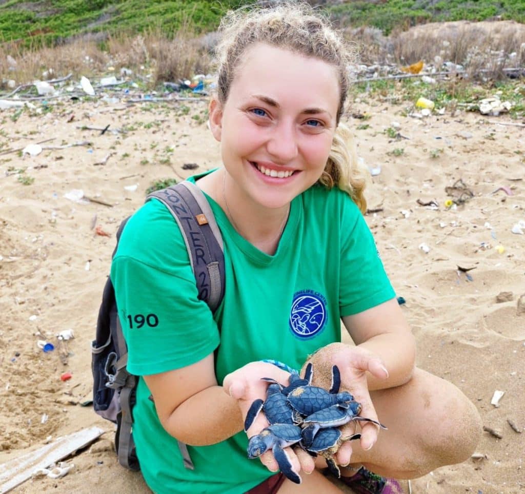 Woman in a green shirt smiling and holding several turtles.