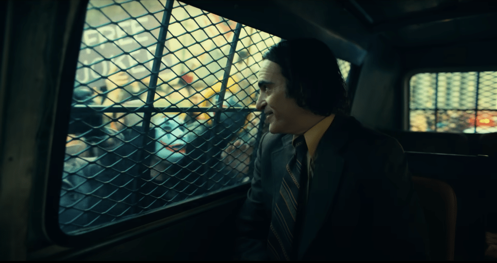 A screenshot of the trailer for "Joker: Folie À Deux" showing the Joker in a police van as people cheer for him.