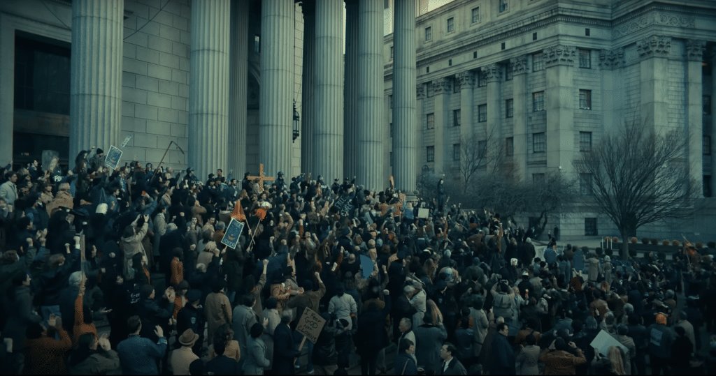 A screenshot of the trailer for "Joker: Folie À Deux," showing a crowd of protestors outside of a city courthouse.