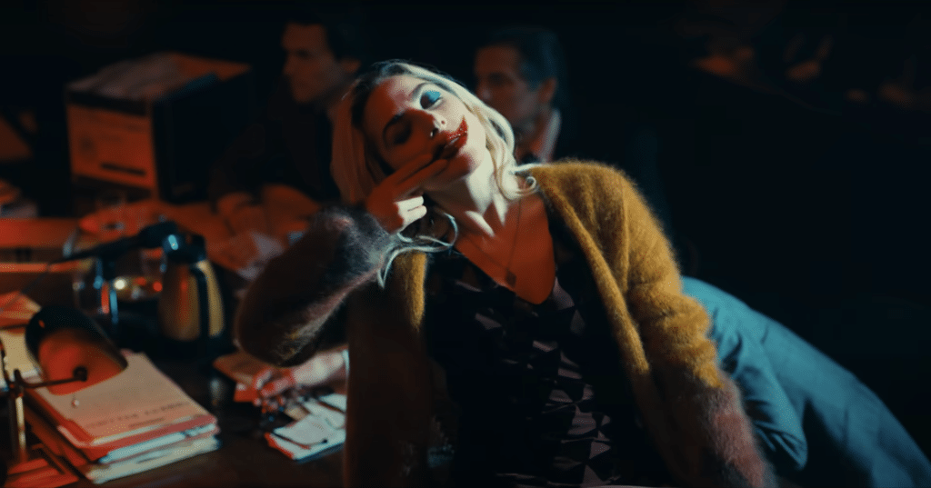 A screenshot of the trailer for "Joker: Folie À Deux" showing Harley Quin painting a smile on her lips with blood.
