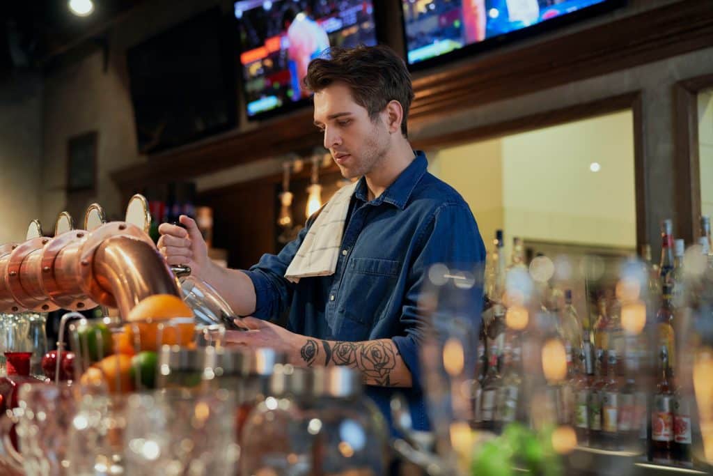 A man pouring a pint of beer behind a bar.